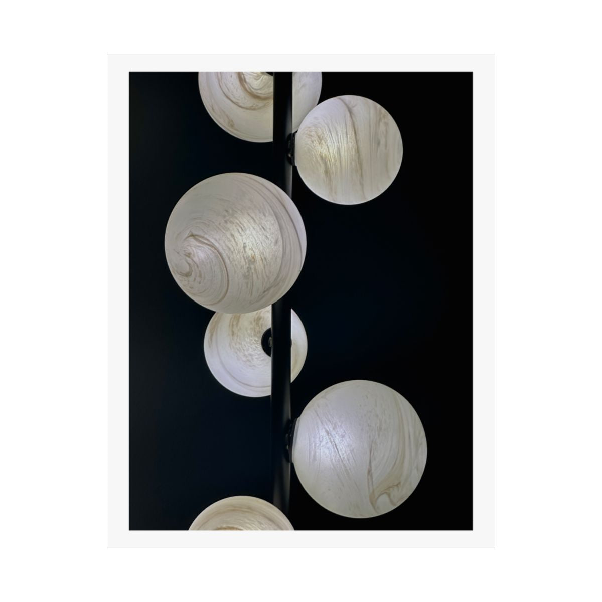 Print of a photograph of pale marbled glass globe lights on a black ground.