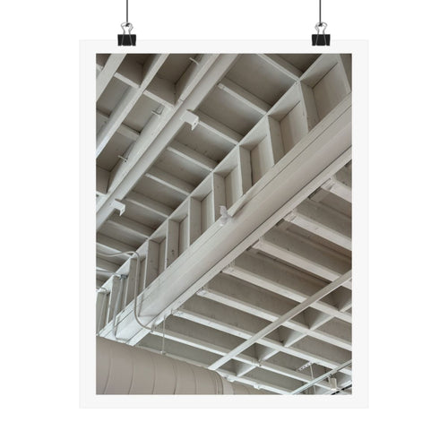 Print of a photograph looking up at white painted ceiling beams and pipework, shown hanging from binder clips.