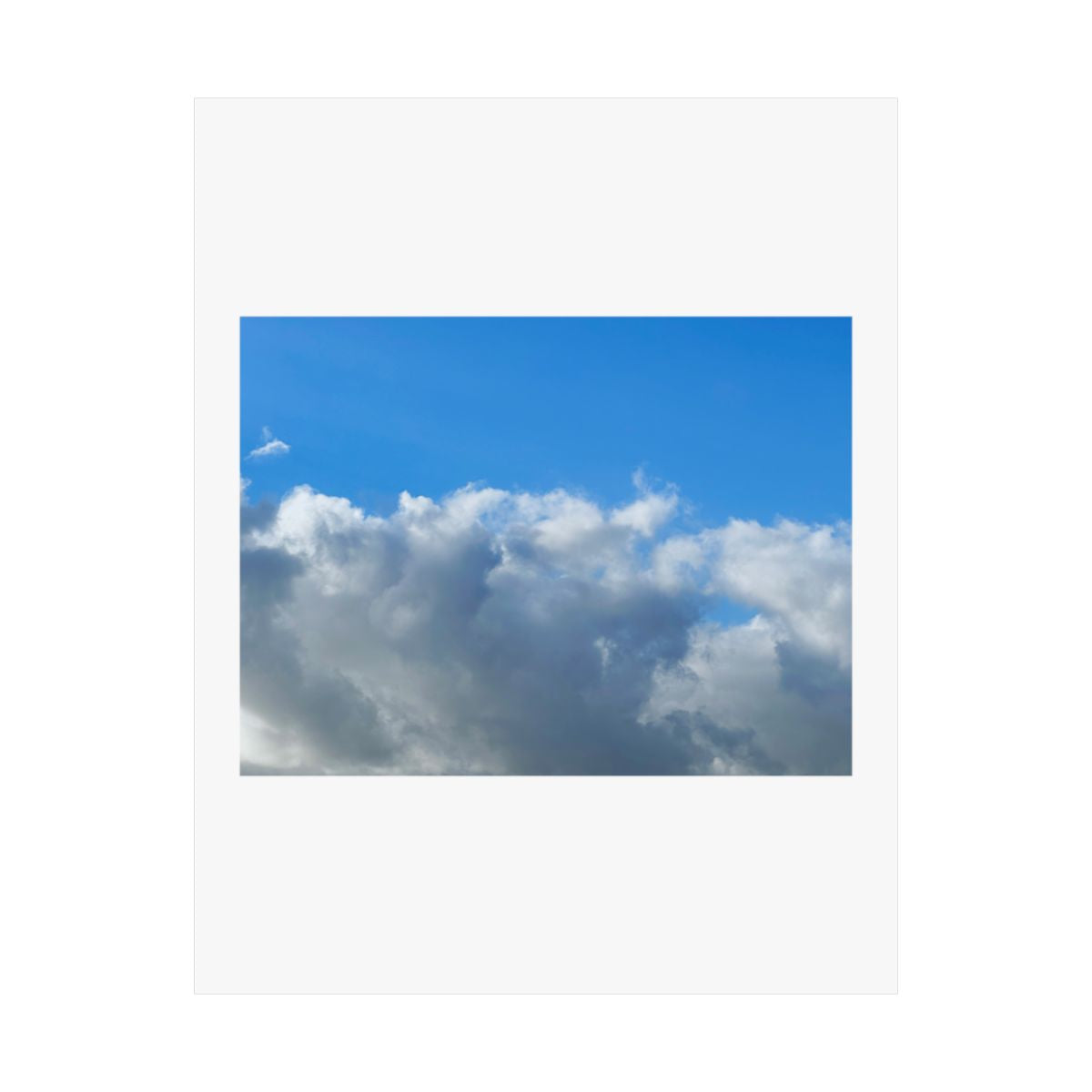 Print of a photograph of a bank of white and grey cloud beneath clear blue sky.