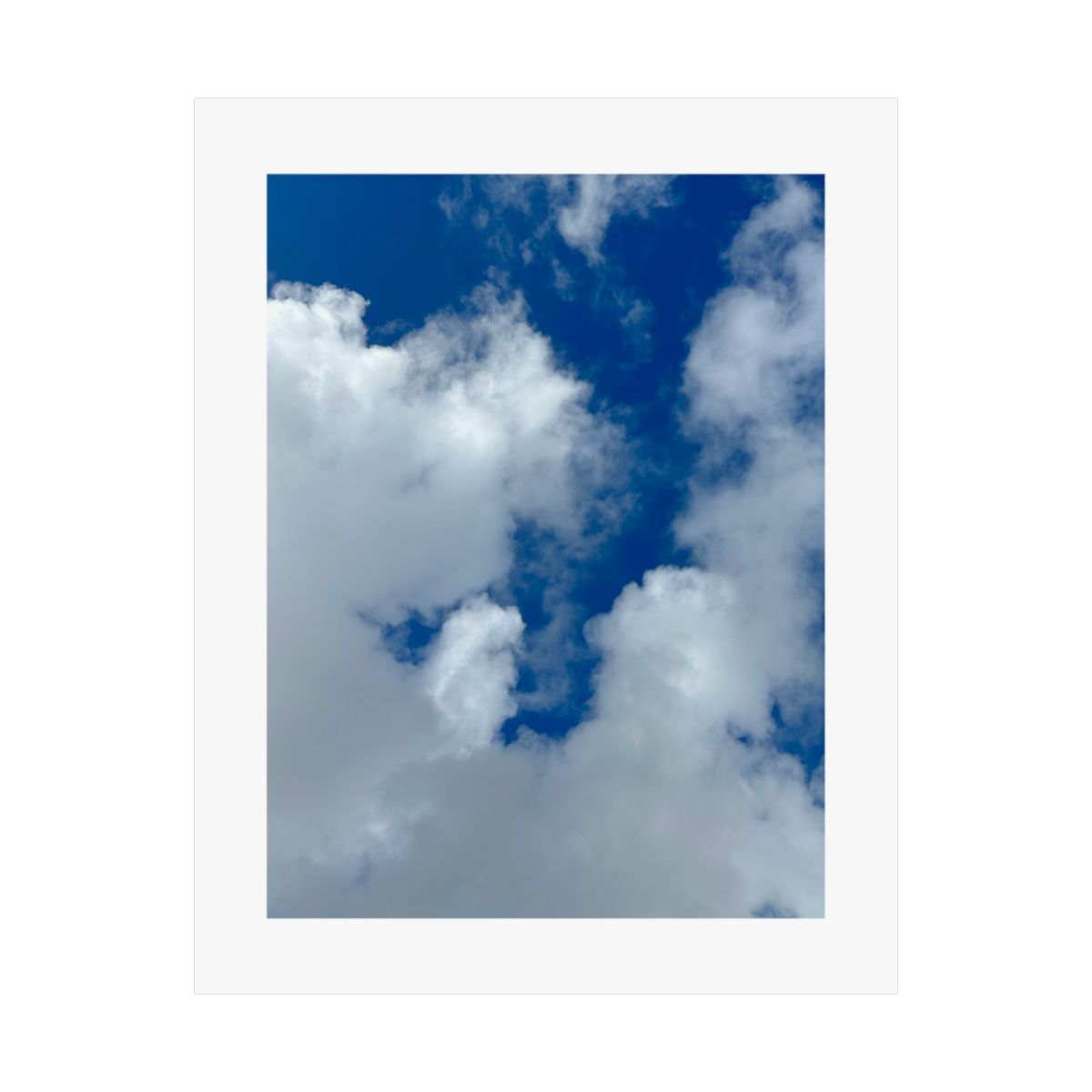 Print of a photograph looking up at bright white clouds against deep blue sky.