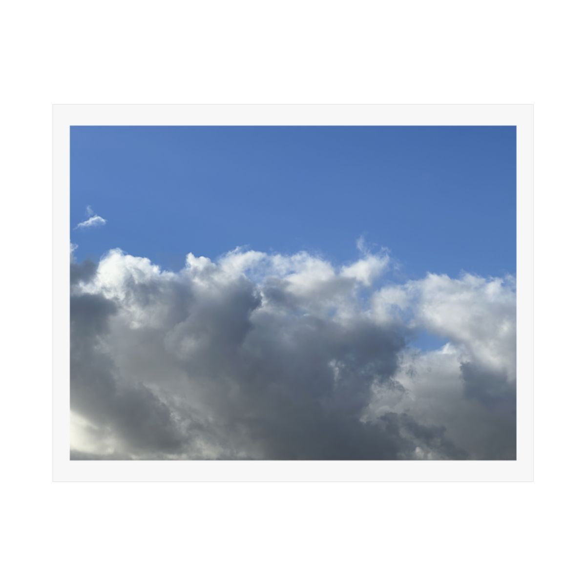 Print of a photograph of a wide bank of white and grey cloud beneath open blue sky.
